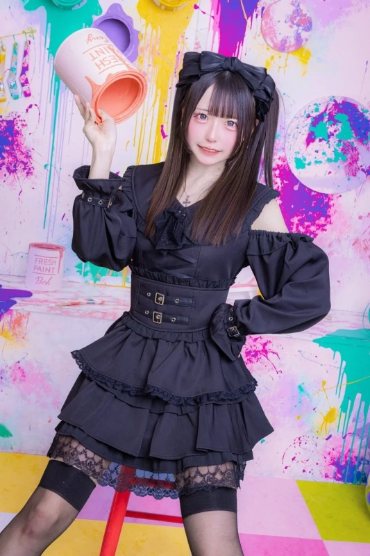 黒いフリルとコルセットの衣装をまとった女性がピンクのペンキ缶を持っている