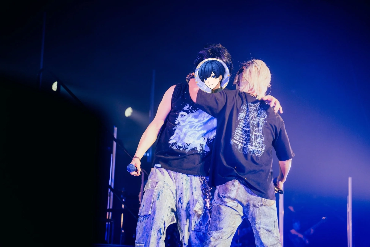 青いステージ照明の下、マイクを持つIfさんと悠佑さんが肩を組み合っている様子