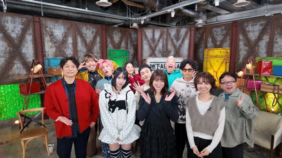 工業的なセットのスタジオで、男女13人のタレントや芸能人が笑顔でポーズをとっている集合写真です。和やかな雰囲気で、番組収録の一場面を捉えたものと思われます。