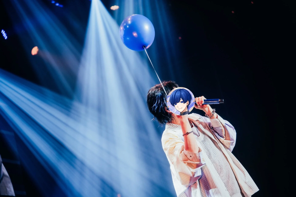 青いスポットライトが照らすステージで、マイクを持ち、青い風船を掲げるIfさんの様子