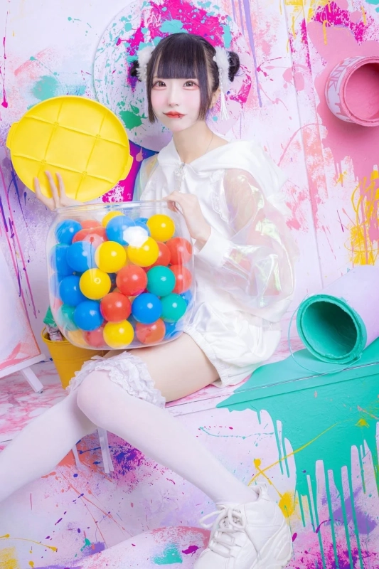 白い衣装をまとった女性がカラフルなボールを抱えている