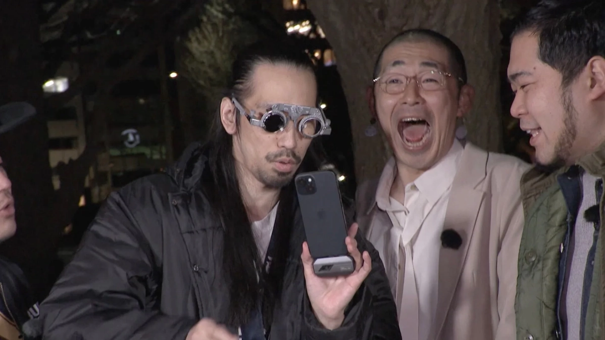 夜の屋外でスマホを見せて笑う男性と爆笑する男性