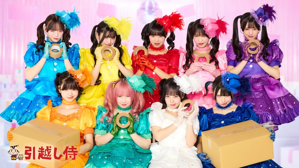カラフルな衣装を着た9人の女性アイドルグループが、引越しをテーマにガムテープや段ボール箱を持ってポーズをとっている広告画像です。明るくポップな雰囲気で、引越し侍のロゴも確認できます。