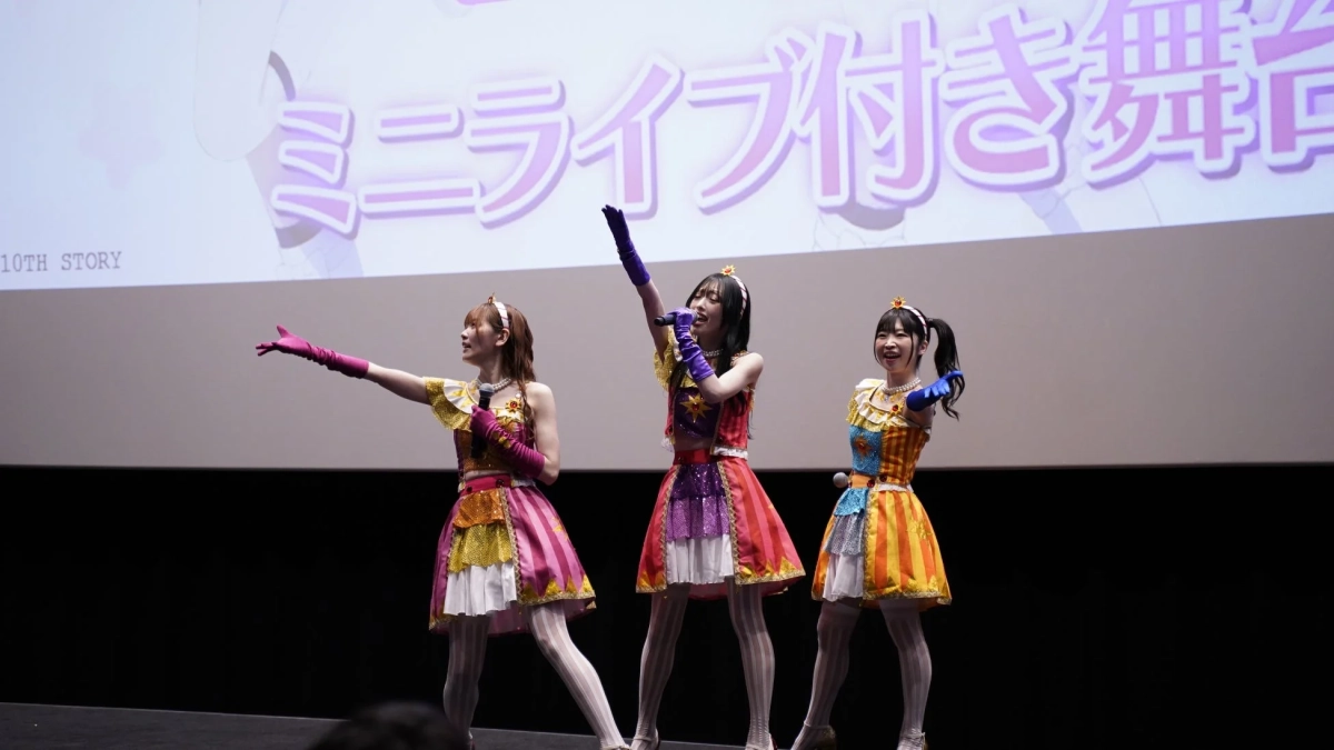 カラフルな衣装をまとった3人の女性パフォーマーがステージ上で歌唱している様子。