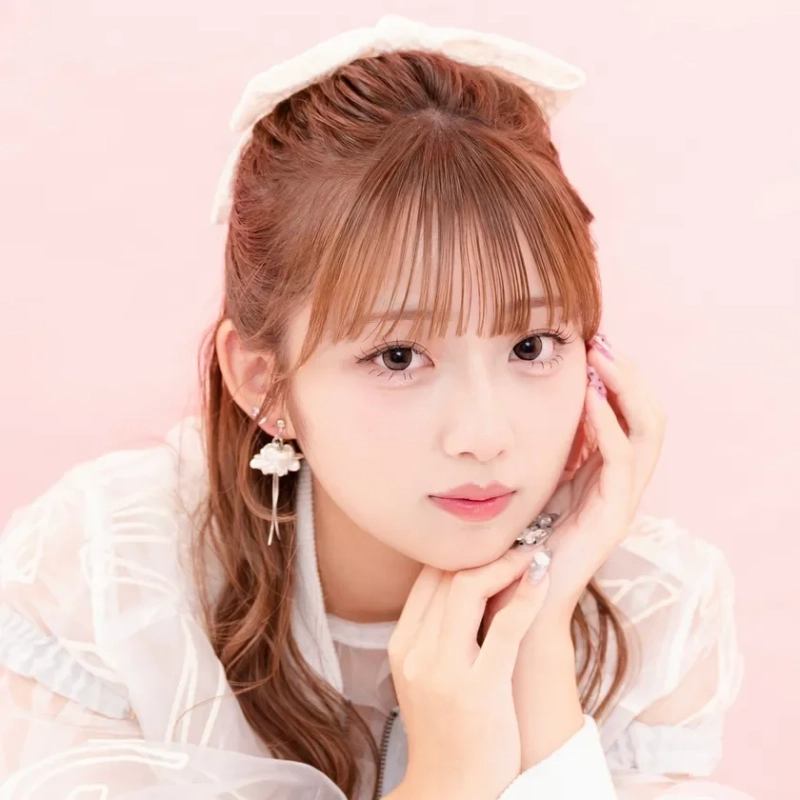 明るいピンクの背景の前で、白い服を着た若い女性がカメラを見つめています。