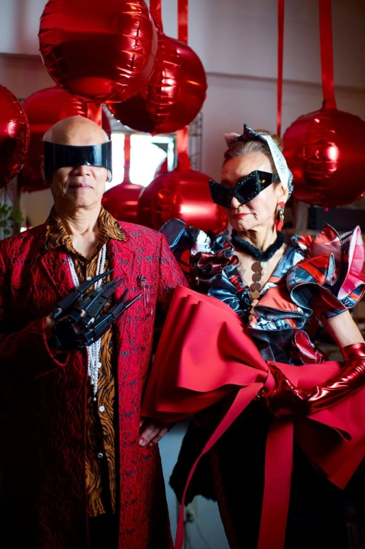 赤い風船を背景に、アバンギャルドで個性的なファッションのシニア男女