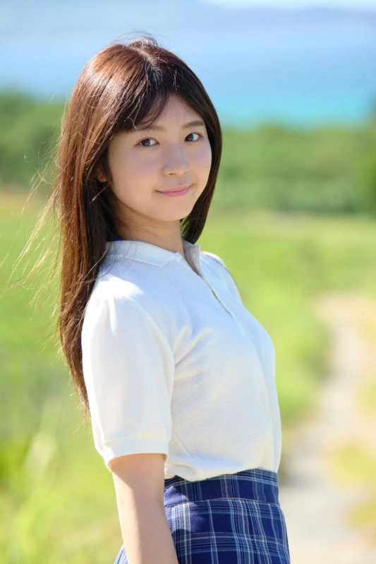 青い空と緑豊かな自然を背景に、白いポロシャツと青いチェック柄のスカートを着た若い女性が優しく微笑んでいます。