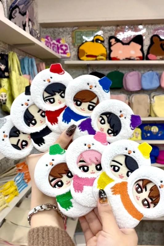 両手で複数の雪だるまの着ぐるみを着た可愛らしいキャラクターグッズを広げている様子