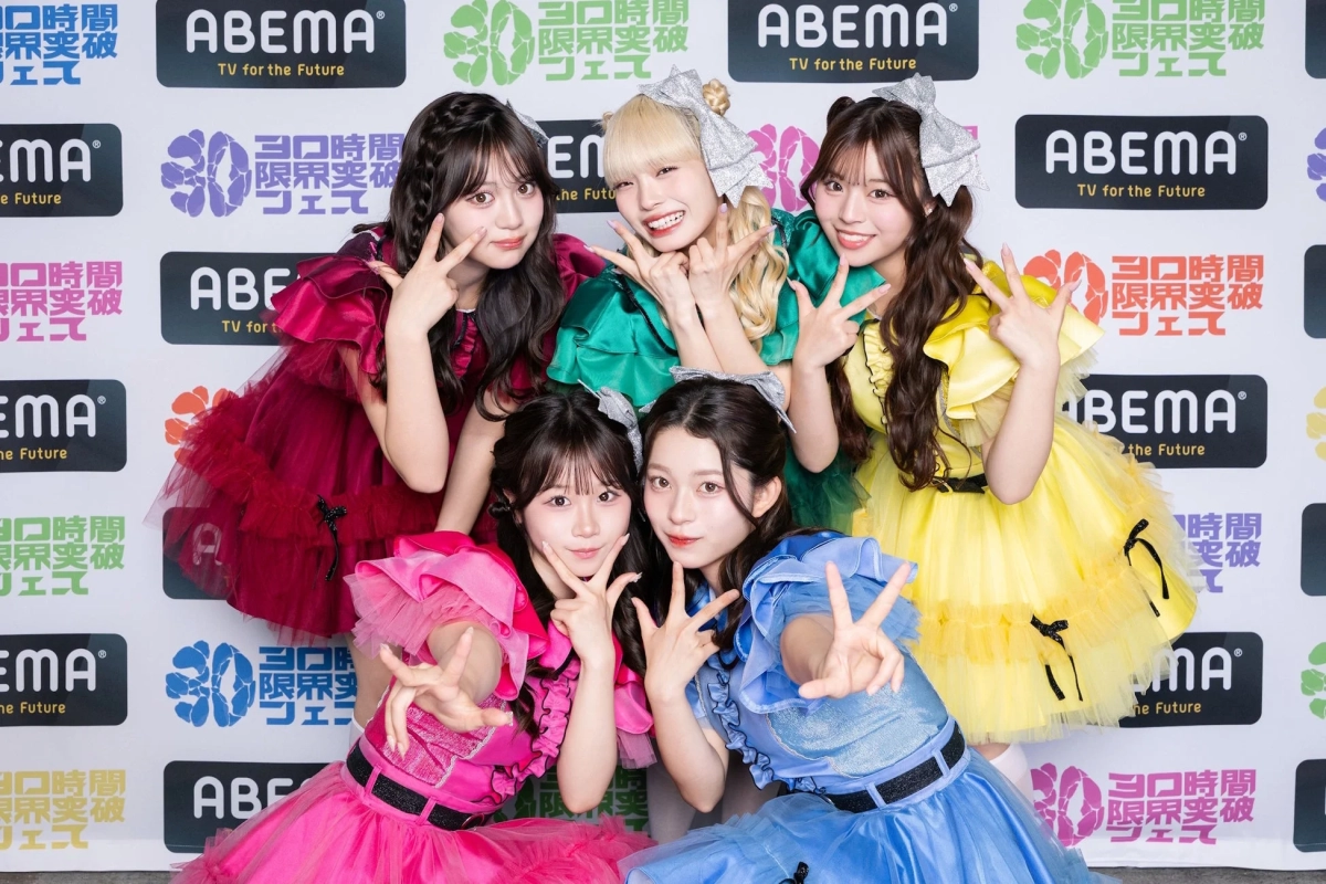 カラフルなフリルドレスを着た5人の若い女性アイドルグループが、ABEMAのイベント「30時間限界突破フェス」のロゴを背景に、笑顔でポーズをとっている様子。