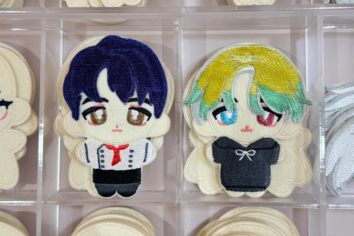 透明なケースに並べられた、アニメ風のデフォルメされたキャラクターの刺繍ワッペン2点