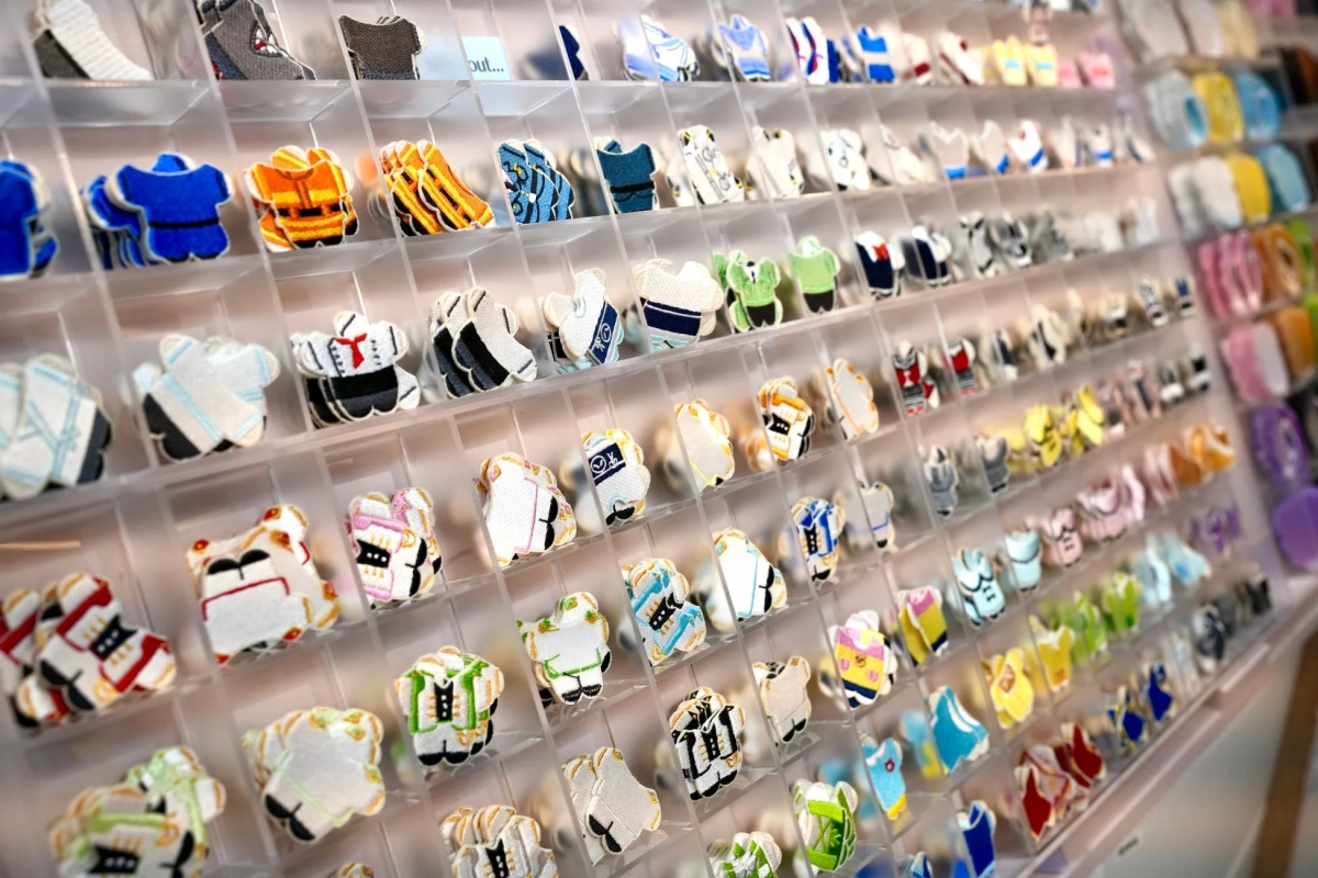 透明な仕切りに多数のカラフルなミニチュア服型ワッペンやエンブレムが整然と陳列されている様子