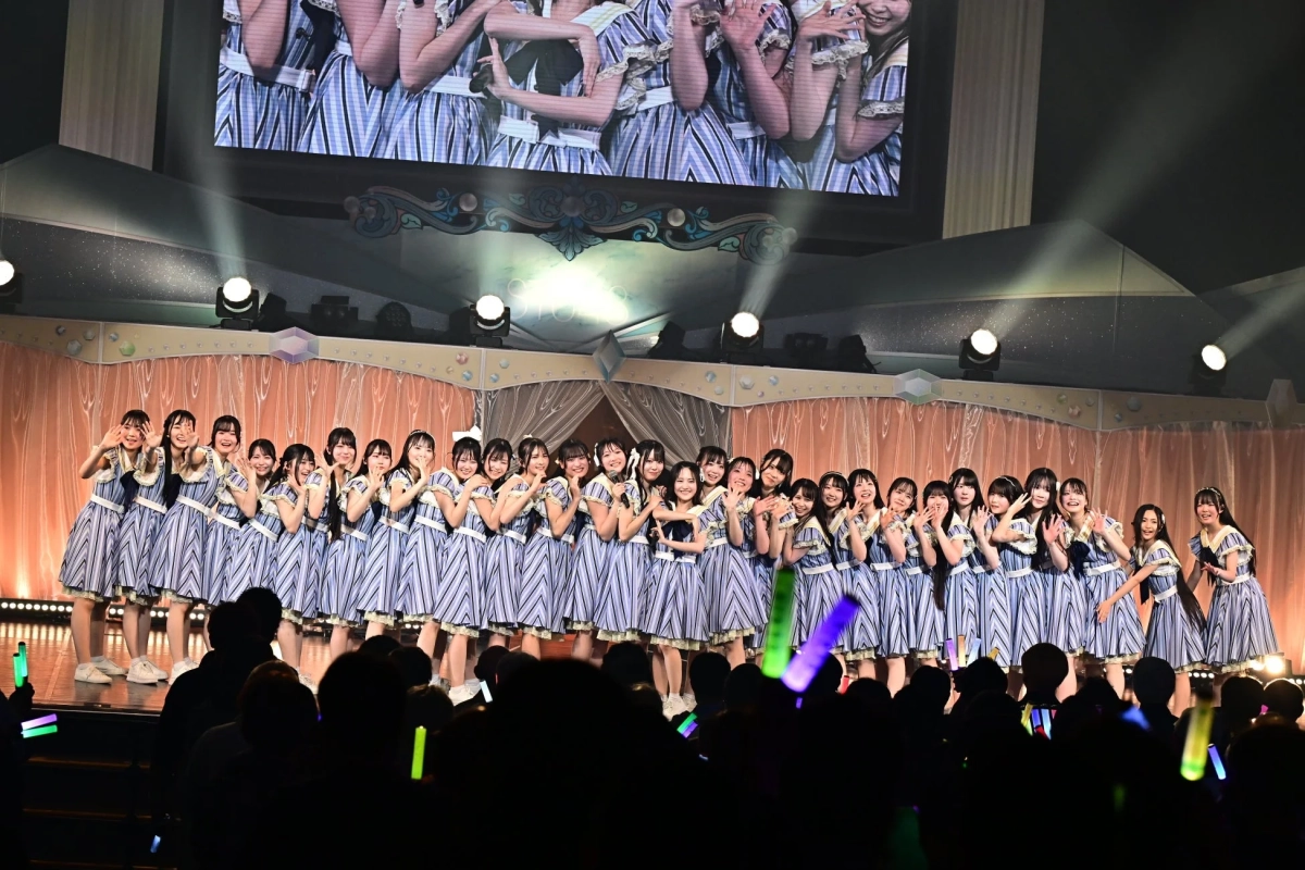 多数の女性アイドルグループがステージ上でストライプの統一衣装を着用しパフォーマンスを行っている