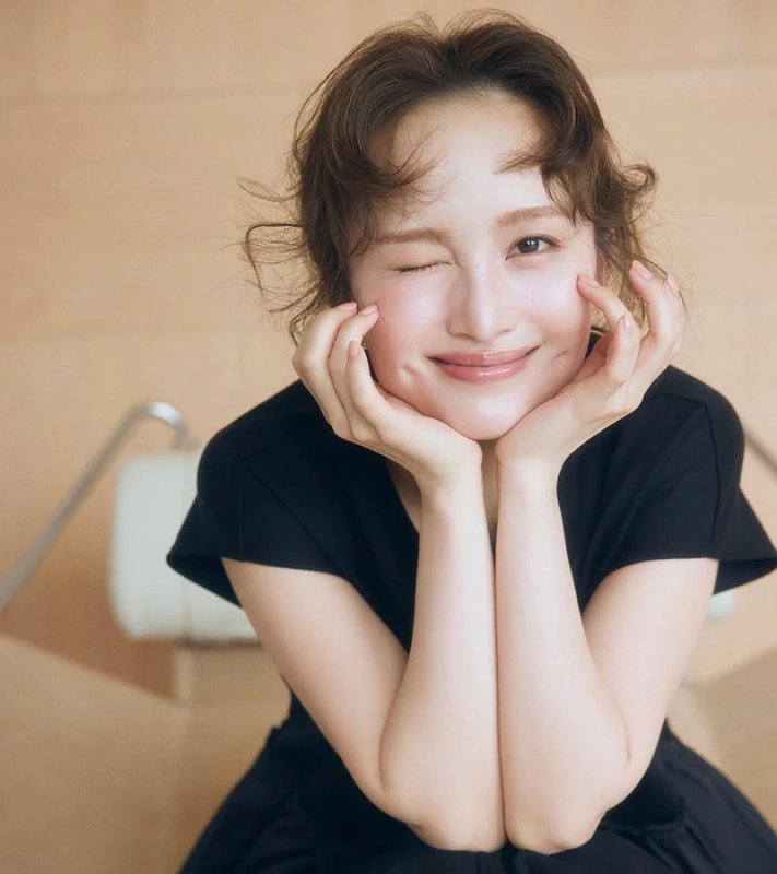 明るい背景の前で、黒い服を着た女性がウィンクをしてにこやかに微笑んでいます