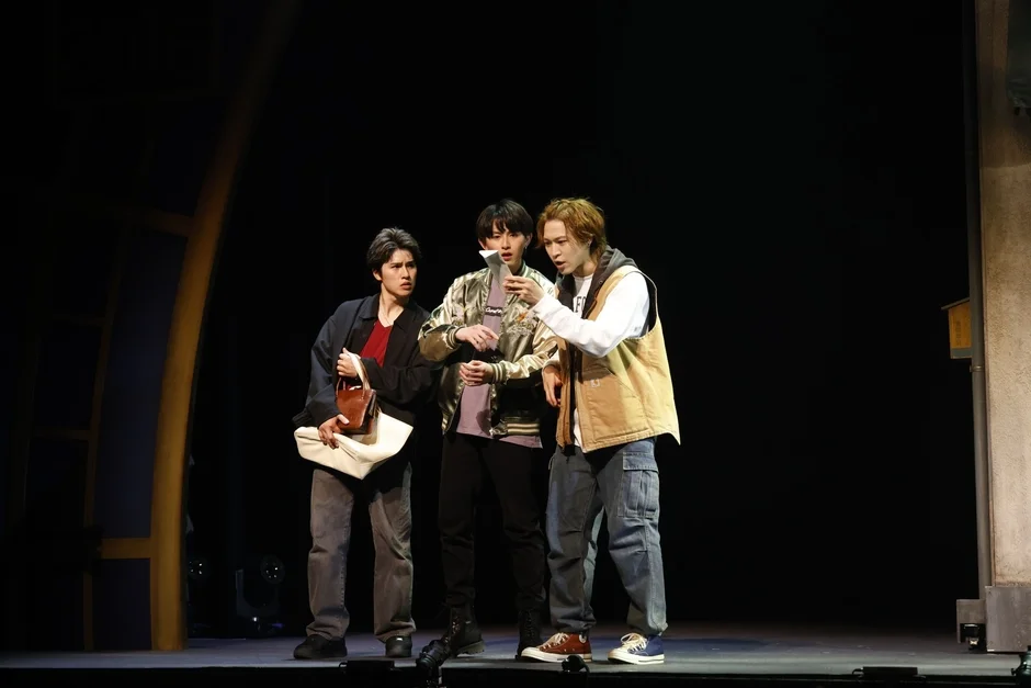 暗い舞台上で3人の男性俳優が演技をしている