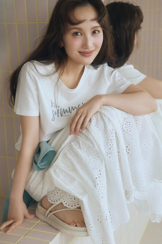 白いTシャツとレースのロングスカートを着た女性が座って微笑んでいます