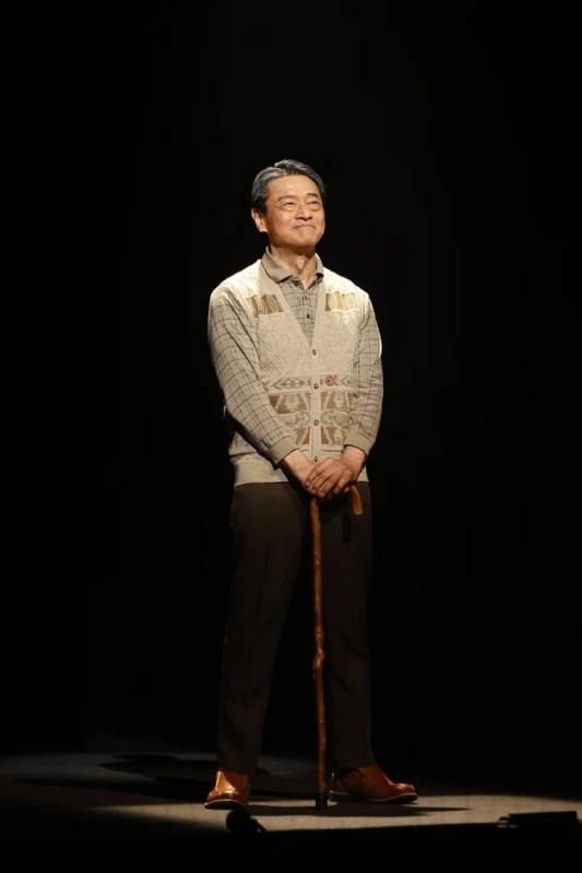 暗い背景の中、スポットライトを浴びて立つ高齢のアジア人男性の全身像