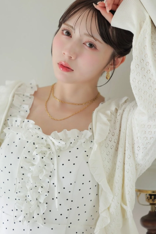 白いドット柄のワンピースとフリル、透かし編みのカーディガンを着用した若い女性のポートレート