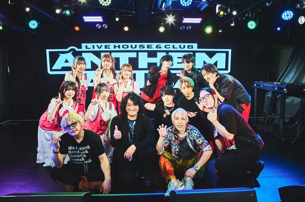 「LIVE HOUSE & CLUB ANTHEM」のロゴが映るステージ上で、多くの男女が集合写真を撮影しています。出演者や関係者が笑顔でポーズをとっており、イベントの成功を祝っているような賑やかな雰囲気です。