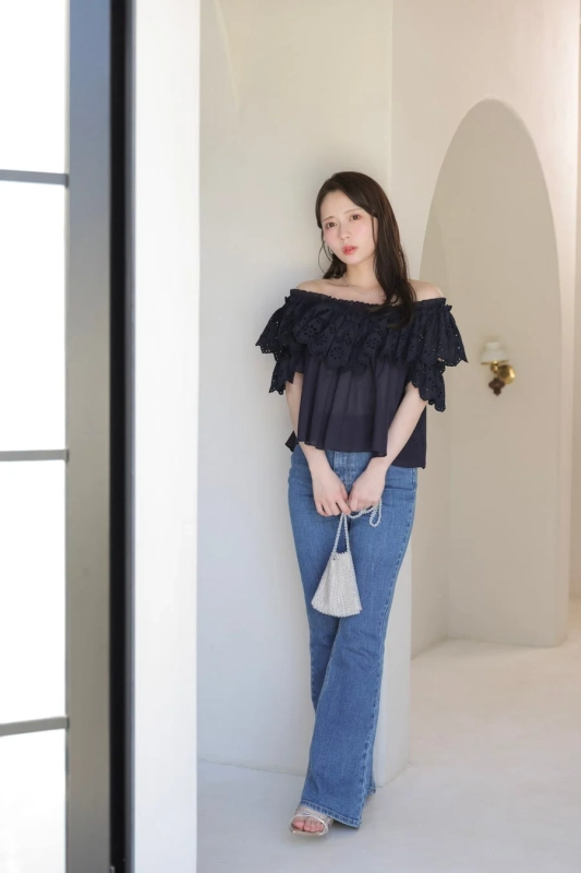オフショルダーの黒いトップスとデニムパンツを着用した若い女性