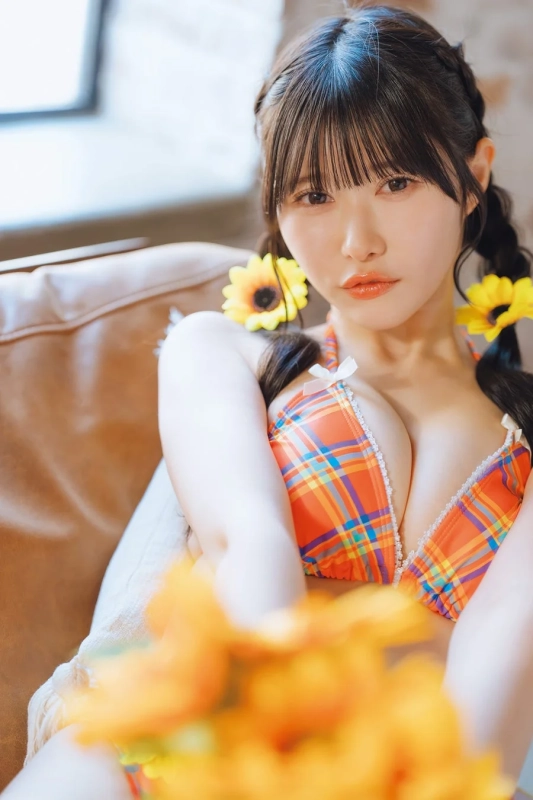 ひまわりの髪飾りをつけた三つ編みの女性が、オレンジ色のチェック柄ビキニを着用