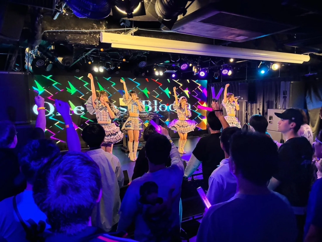 ライブハウスで歌手がステージに立ち、熱気あふれるパフォーマンスを披露しています。