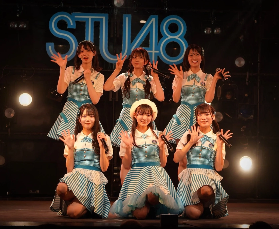STU48のメンバー6人が、青と白のストライプ柄の衣装を着てステージ上でポーズをとっています。マイクを持ち、笑顔で手を振っており、背景にはSTU48のロゴが見えます。
