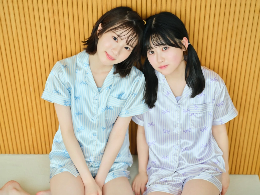 パジャマ姿の若い女性が2人、木製の壁を背景に並んで座っている写真