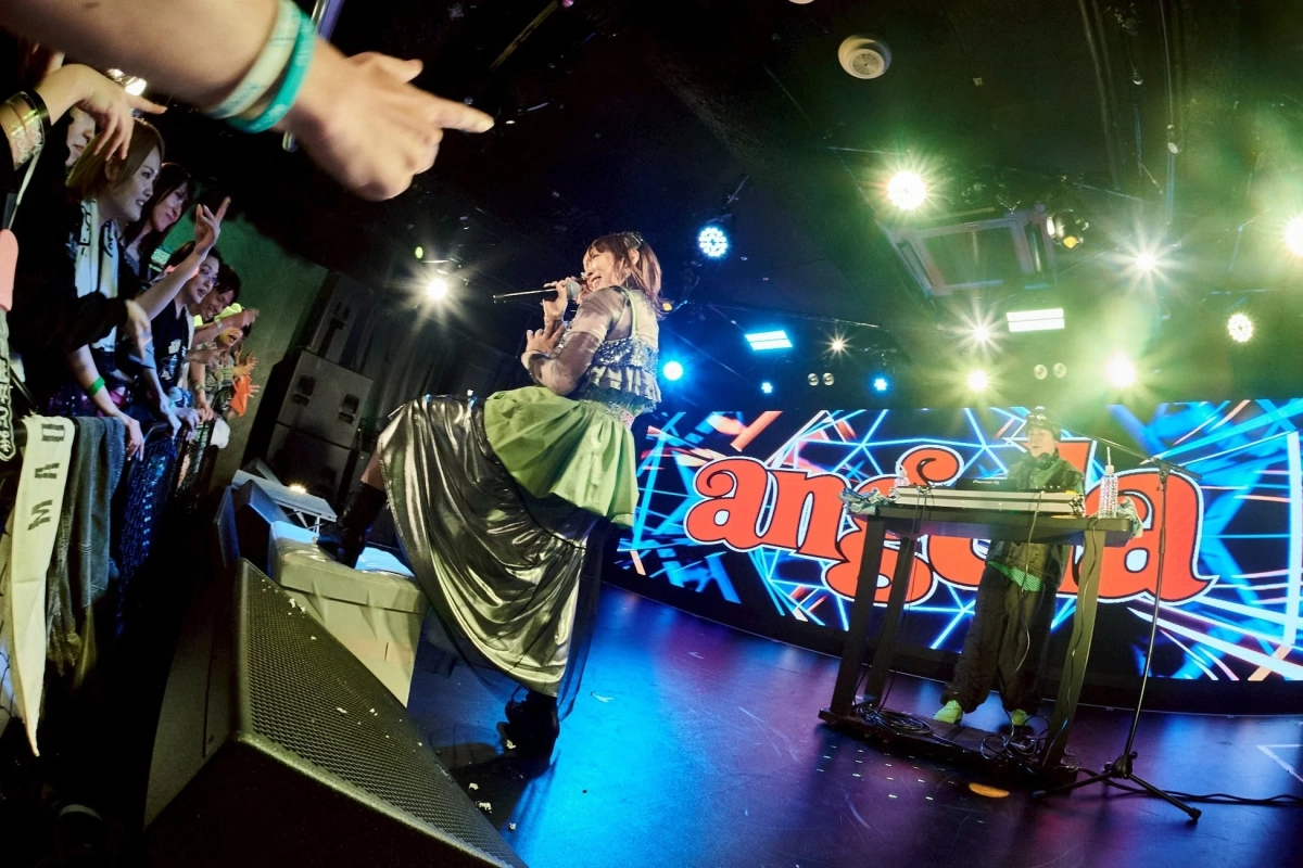 華やかな照明に照らされたライブステージで、女性歌手が熱唱し、DJが演奏している様子。背景には「anison」の文字が表示され、観客も手を上げて盛り上がっており、エネルギッシュなライブパフォーマンスが伝わる一枚。