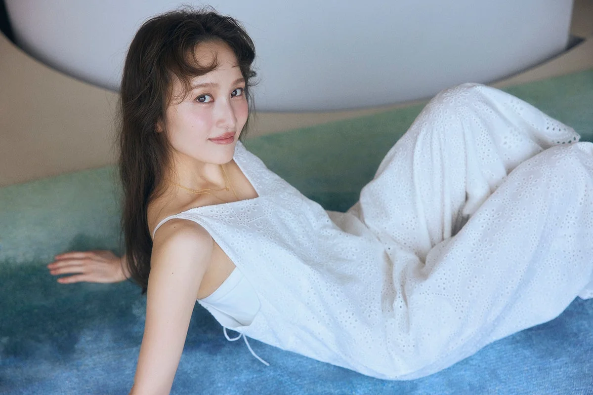 白い透かし編みのワンピースを着た日本人女性が、笑顔でリラックスした表情で横たわっているポートレート写真