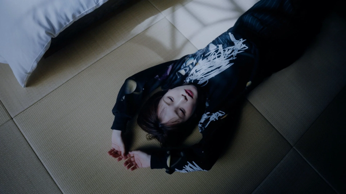 畳の上に横たわる女性の姿を上から捉えた画像です。女性は黒い長袖の服を着て目を閉じ、リラックスしているように見えます。