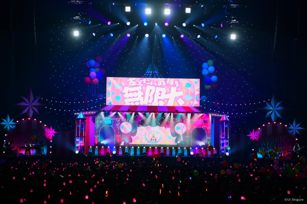 カラフルな照明とサーカス風の装飾が施されたコンサートステージで、熱気あふれるライブが開催されています。