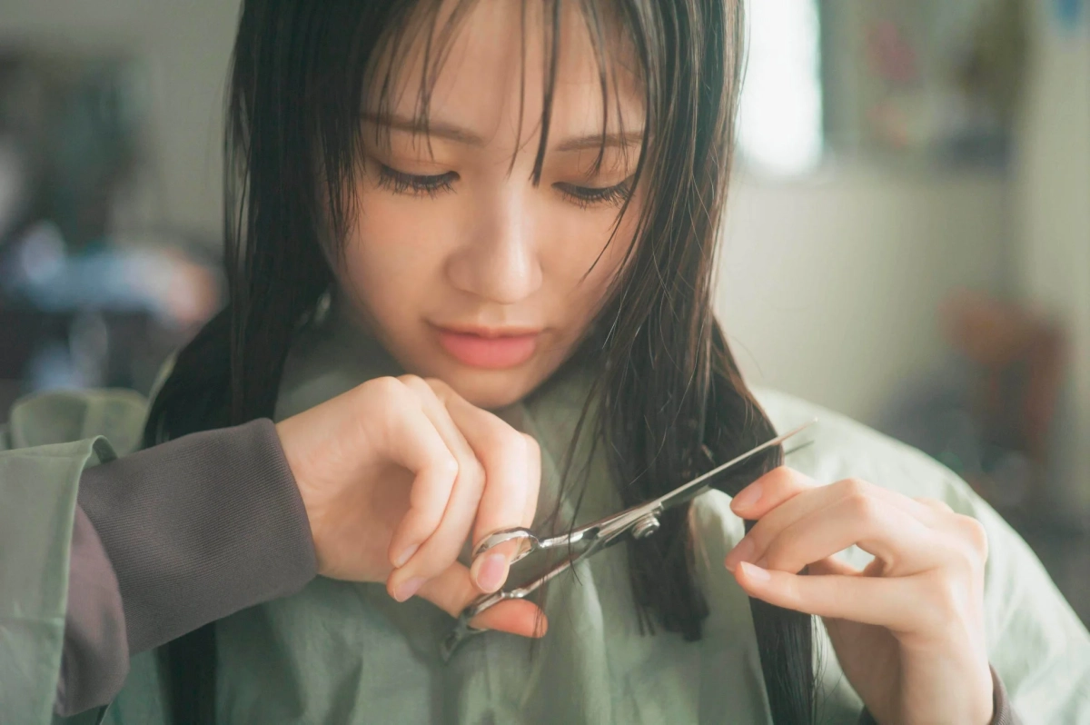 若い女性が自分で髪を切っている様子を捉えた画像です。真剣な表情でハサミを使い、自身の髪の毛をカットしています。