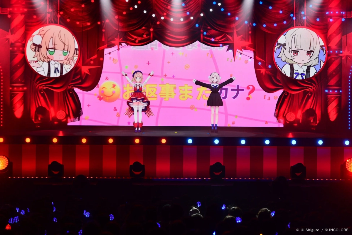 2体のバーチャルキャラクターがステージでパフォーマンスし、観客がペンライトを振るライブイベントの様子。
