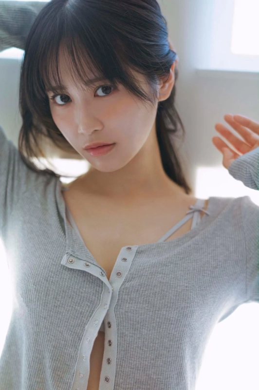 自然光が差し込む室内で、カメラをまっすぐ見つめる若い女性のポートレート。グレーのリブ編みトップスを着て、両腕を頭の後ろに上げ、リラックスしたポーズをとっている。清楚で穏やかな雰囲気が感じられる一枚。