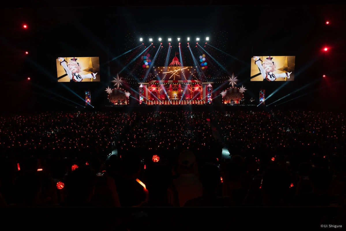多数の観客がペンライトを振る中、サーカステントを模した華やかなステージでバーチャルアイドルのライブが行われています。