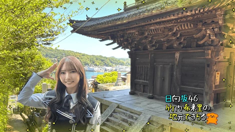 寺院と港町を背景に笑顔で敬礼する日向坂46竹内希来里さん