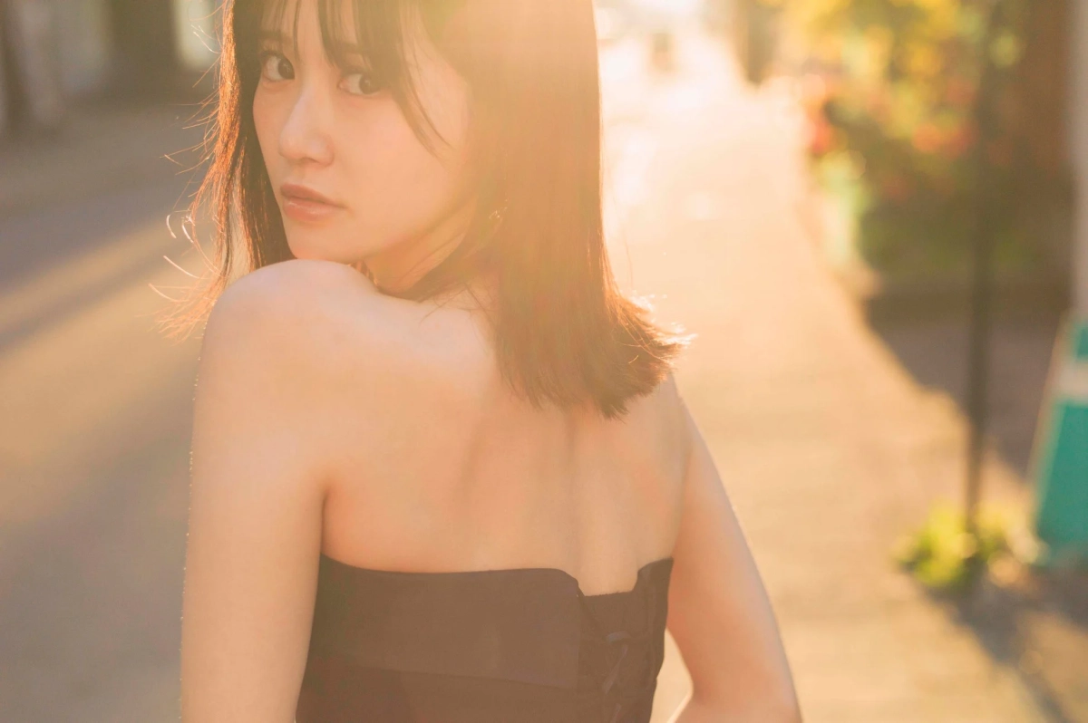 夕焼けのような暖かい光の中で、カメラを振り返る若い女性のポートレートです。肩を出した黒い衣装を着用し、柔らかな表情と美しい肌が印象的な一枚です。