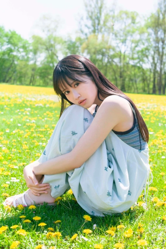 明るい日差しの下、一面に咲くタンポポ畑で座っている若い女性のポートレートです。彼女はカメラを見つめ、穏やかな表情をしています。