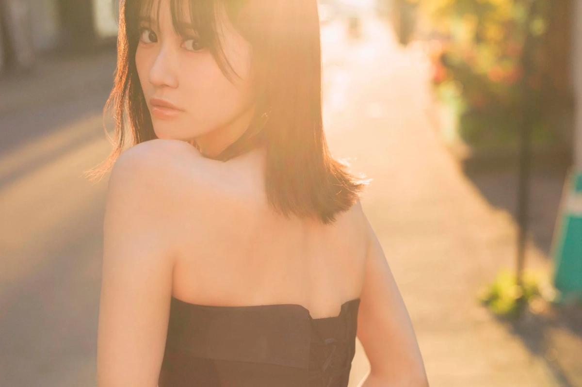 夕焼けのような暖かい光の中で、カメラを振り返る若い女性のポートレートです。肩を出した黒い衣装を着用し、柔らかな表情と美しい肌が印象的な一枚です。
