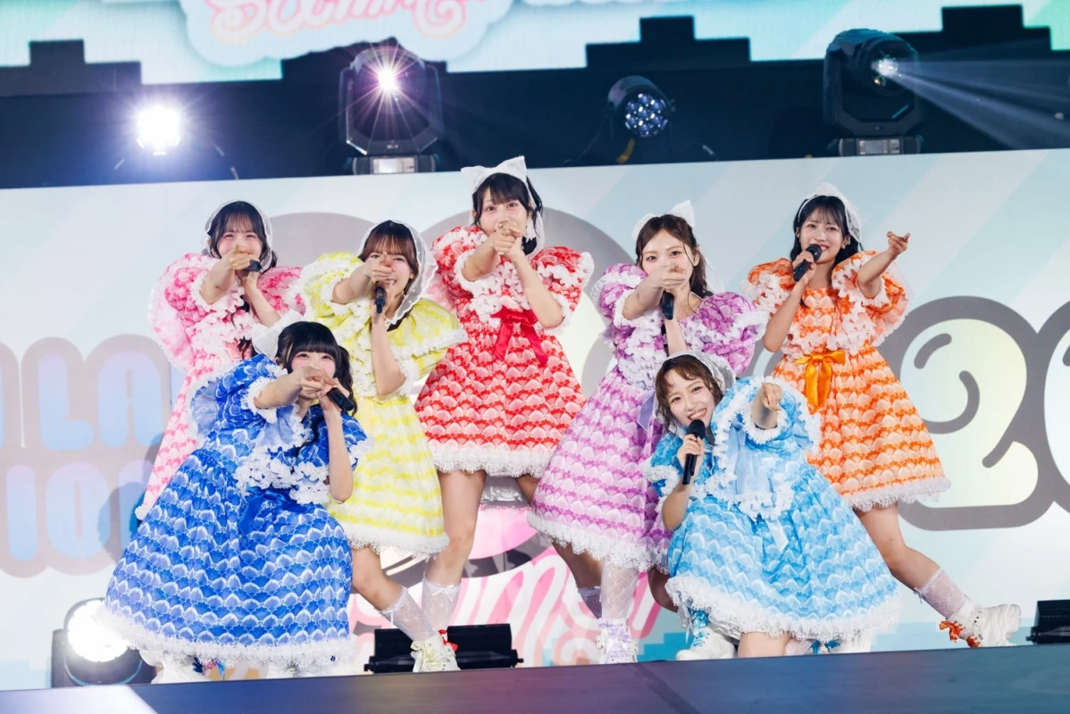 カラフルな衣装をまとったアイドルグループのライブパフォーマンス