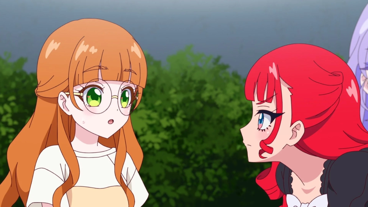 アニメのワンシーン。オレンジ髪で眼鏡をかけた少女が驚いた表情で、赤い髪の少女が真剣な面持ちで向かい合っている。屋外での会話の一場面。