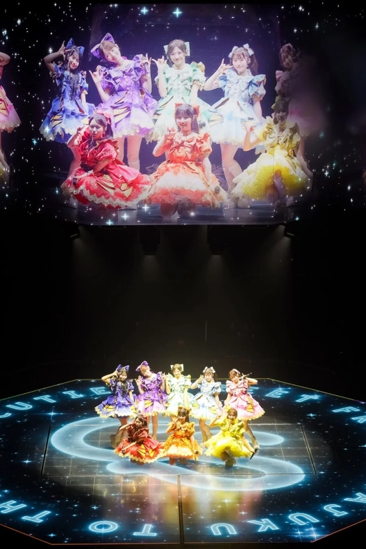 光る文字と模様が描かれたステージでパフォーマンスするアイドルグループ
