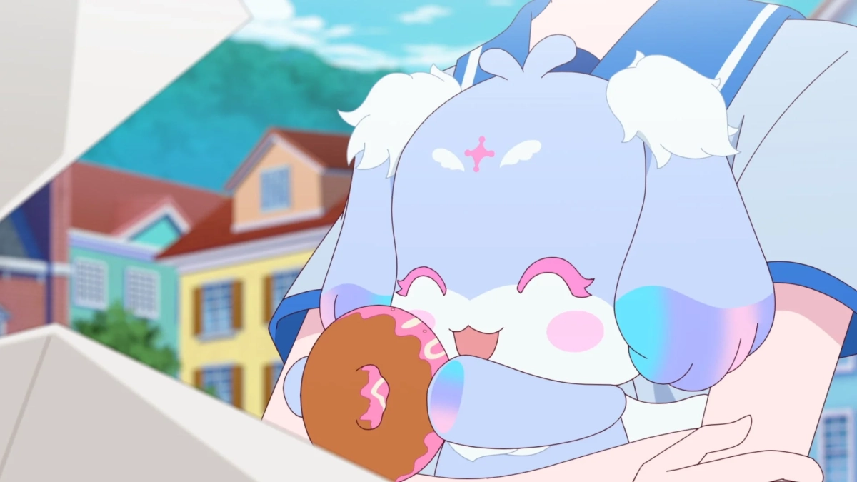 パステルカラーの可愛らしいキャラクターが、ピンクのアイシングがかかったドーナツを抱えて満面の笑みを浮かべているアニメーションの画像です。背景にはカラフルな建物が並ぶ街並みが描かれています。