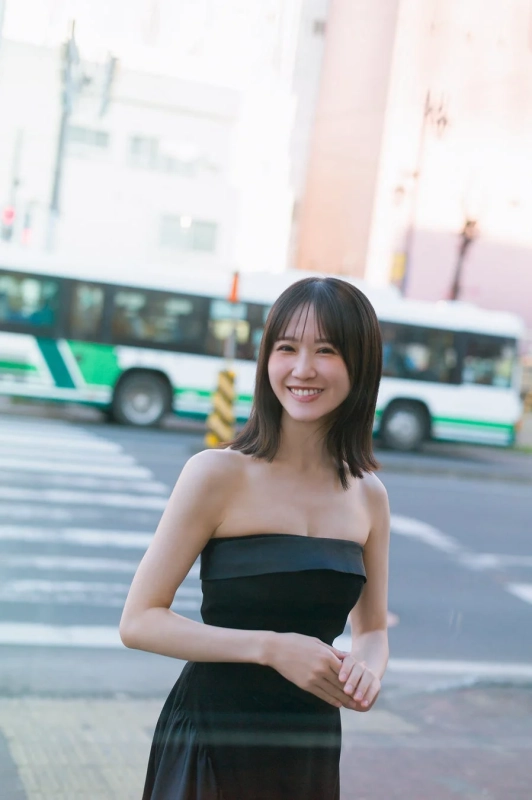 黒いベアトップドレスを着た若い女性が、街中の横断歩道で笑顔を見せているポートレート。