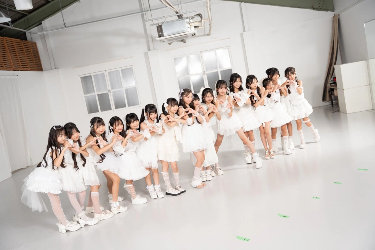 白いドレスを着た大勢の少女たちが、スタジオでハートのポーズを取って並んでいます。
