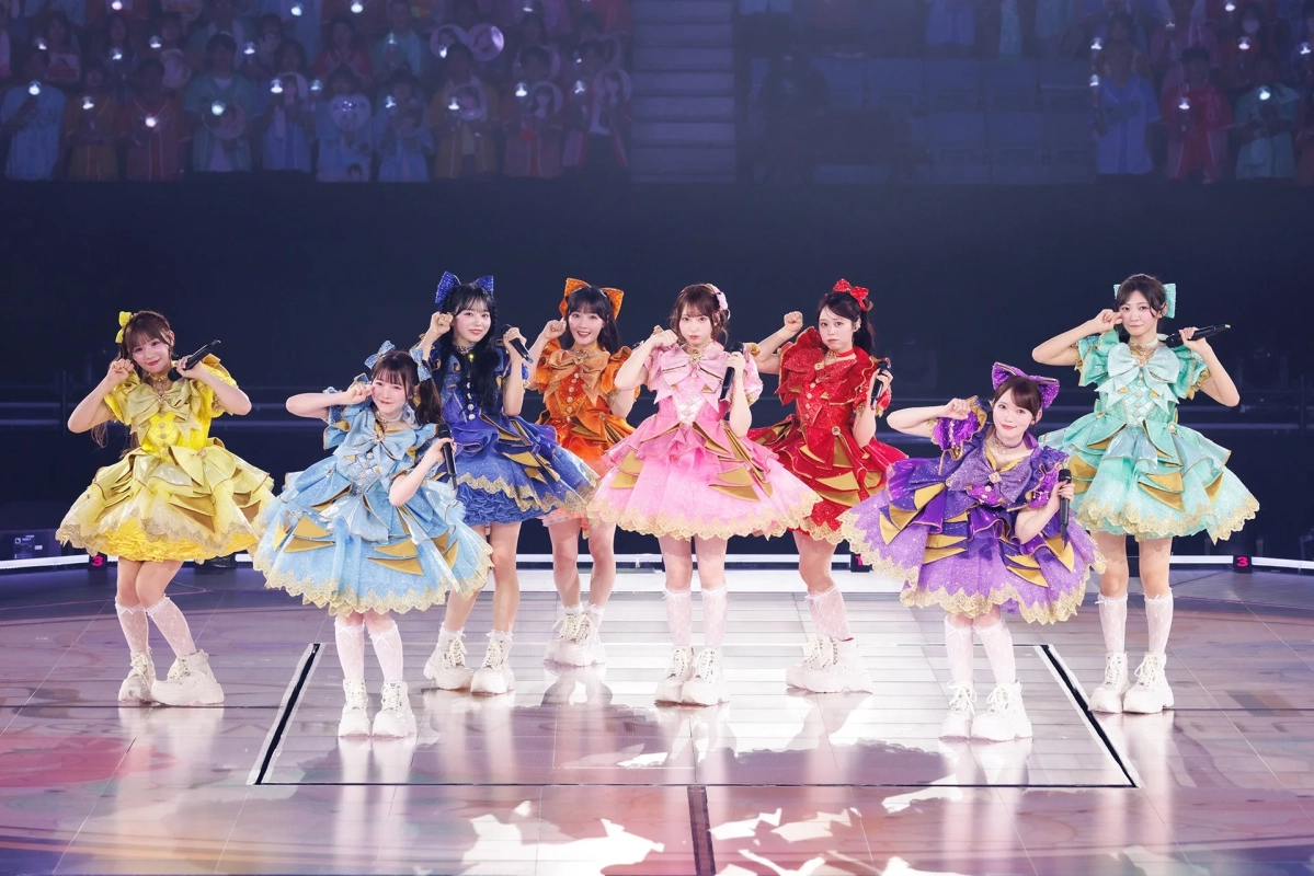 華やかなフリルのドレスをまとった8人の女性アイドルがステージでパフォーマンス