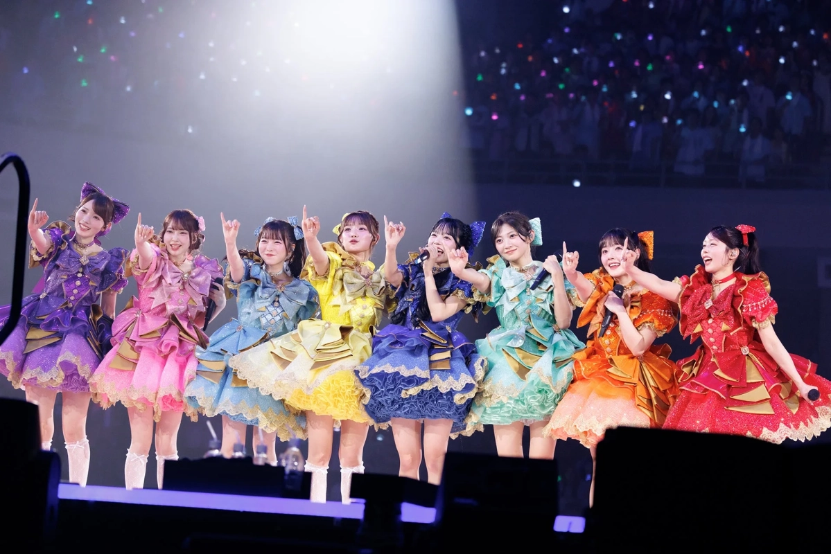 カラフルなアイドル衣装をまとった8人の女性グループがステージでパフォーマンス