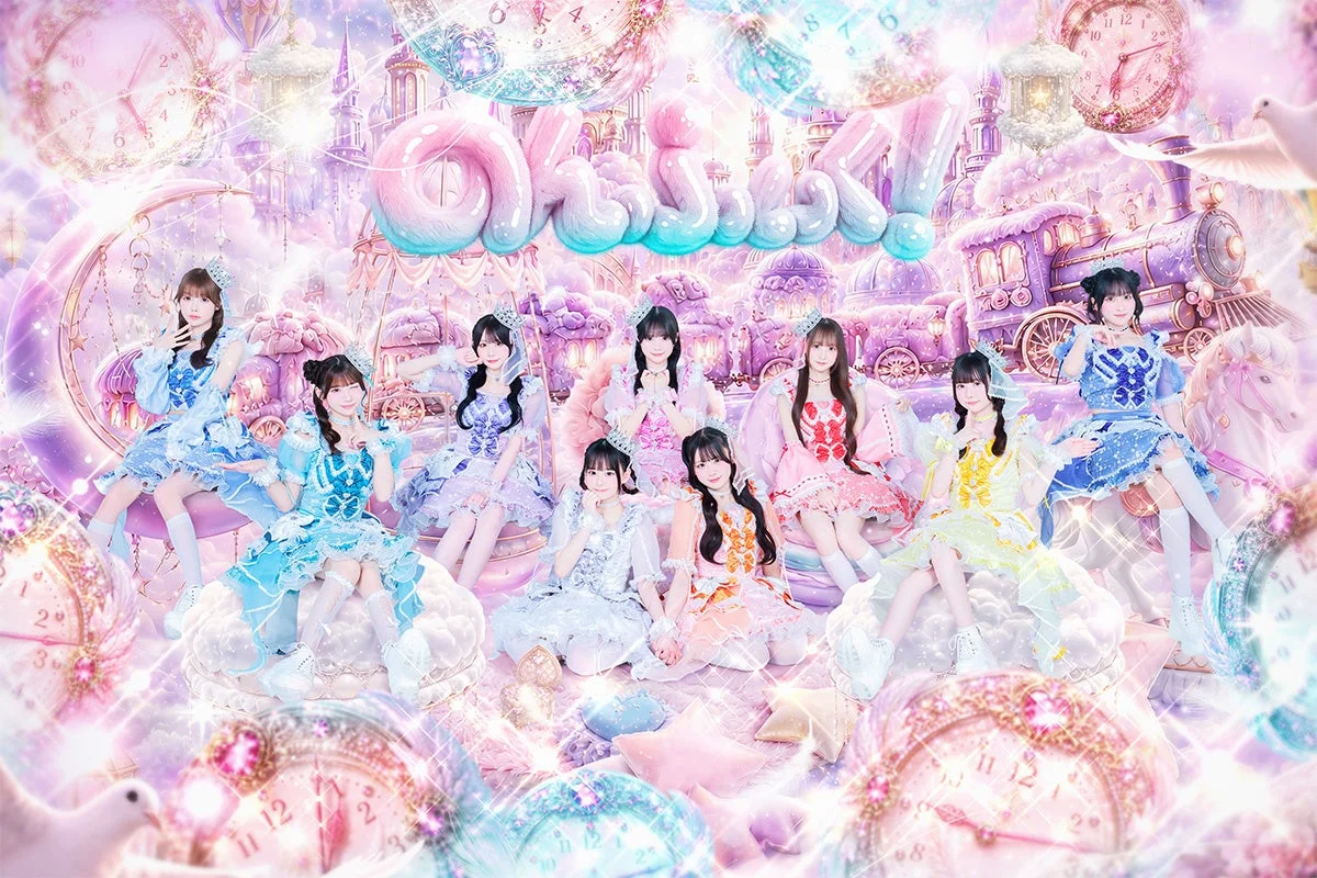 パステルカラーのファンタジーな世界観で、色とりどりのドレスをまとった9人の女性アイドルグループがポーズをとっています。お城や時計、列車などが描かれ、全体的にキラキラとした夢のような雰囲気です。