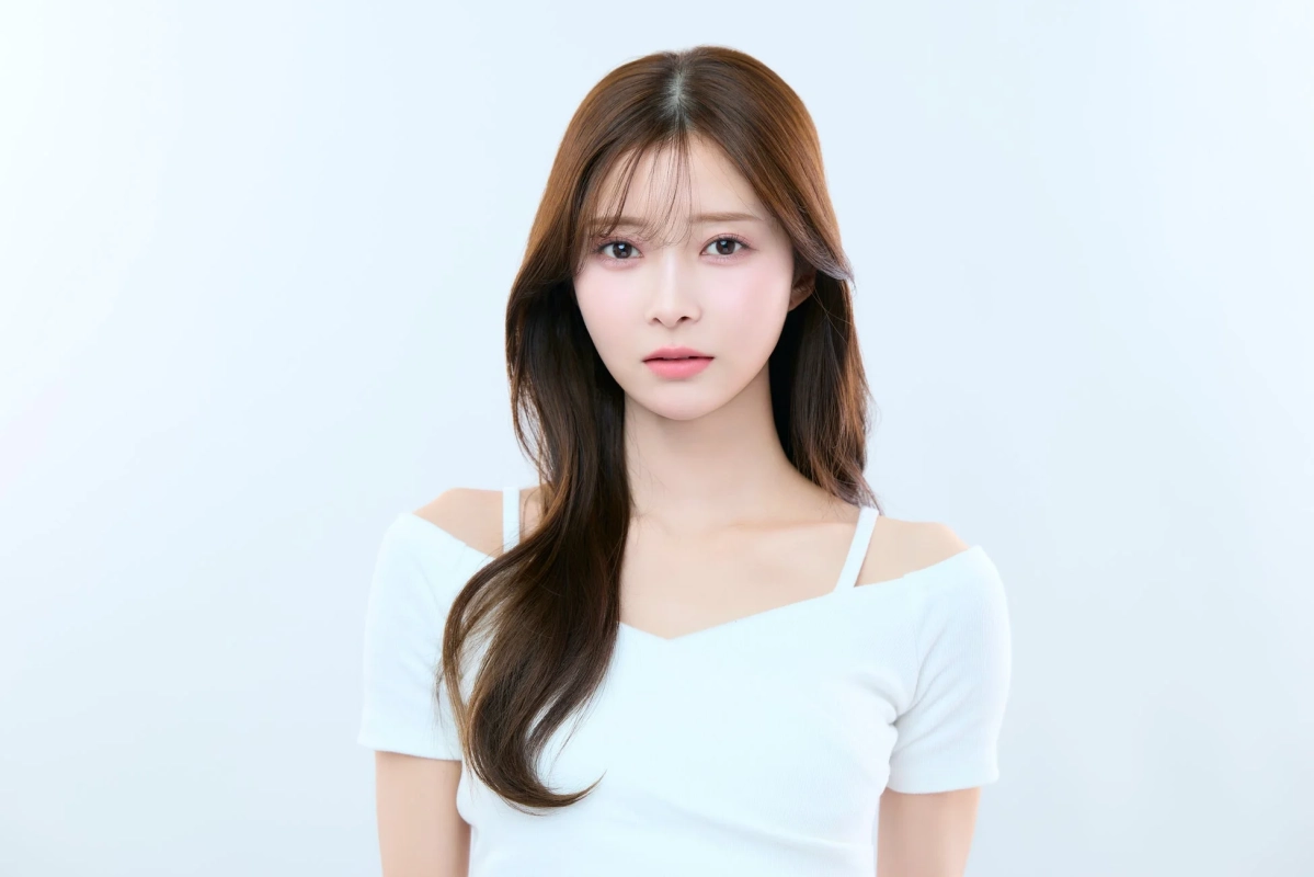 白いオフショルダーのトップスを着た若い女性のポートレート。長い茶色の髪が特徴で、優しい表情でカメラを見つめています。