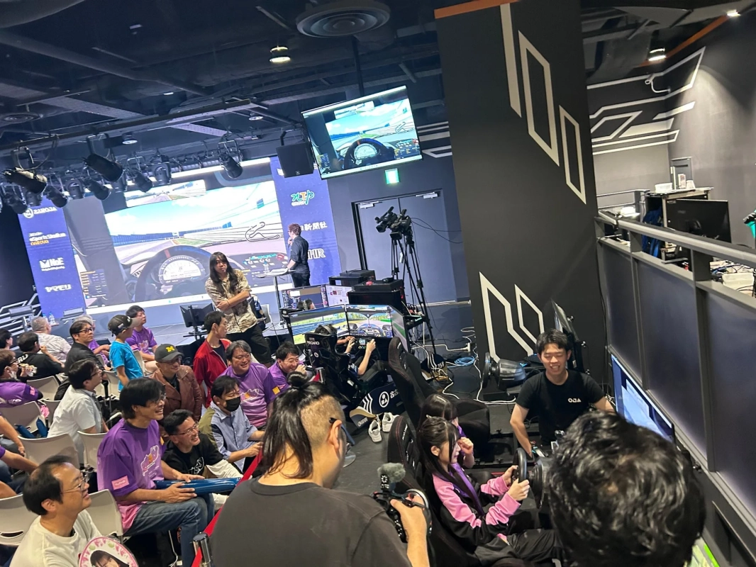 eスポーツイベントの様子。大勢の観客が見守る中、レーシングシミュレーターでゲームを楽しむ参加者たちが映し出されています。